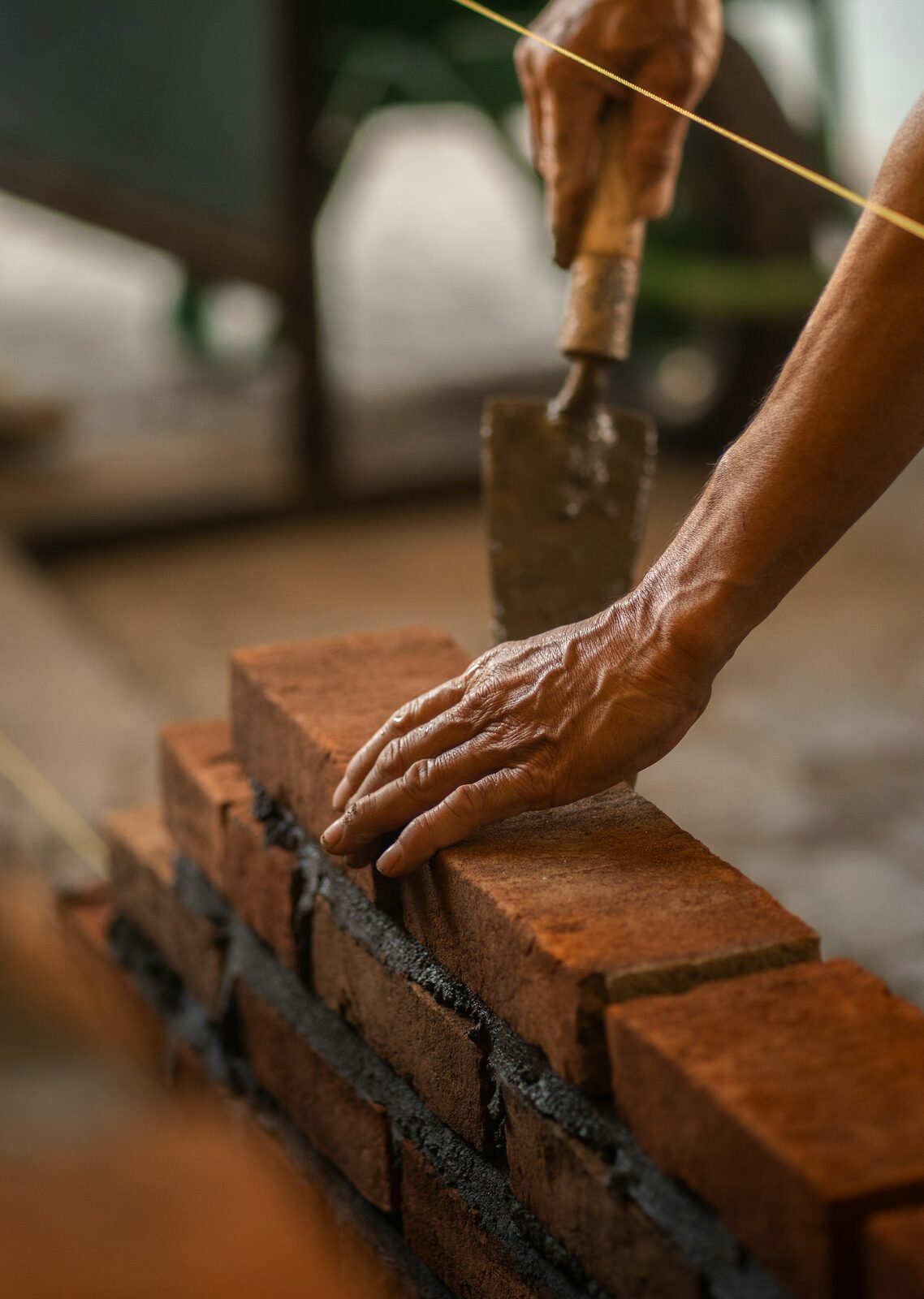 Bricklayer setting a brick on a string line, close detail of the trade